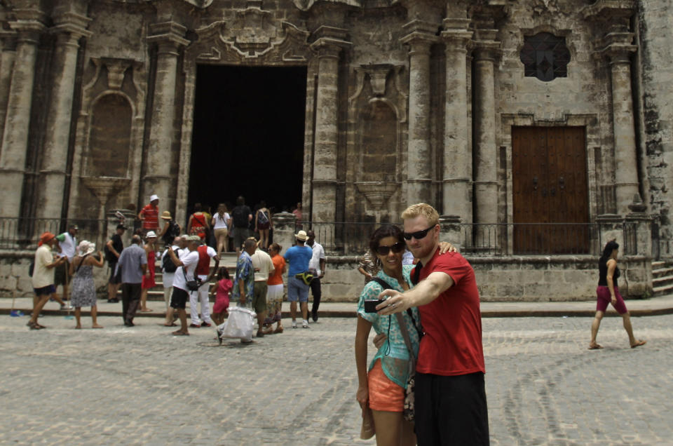 In this July 10, 2013 photo, tourists take photos of themselves outside the Cathedral in Havana, Cuba. For a place where most people earn just $20 a month at their government jobs, Havana can be a surprisingly expensive place to be a traveler. But there are plenty of free ways to have fun in this city known for sea, sun and salsa. (AP Photo/Franklin Reyes)