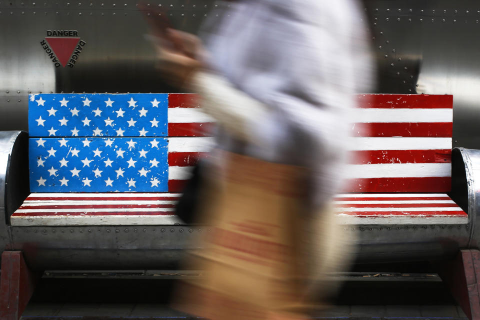 In this Sunday, Jan. 6, 2019, photo, a woman walks by a bench painted with the U.S. flag at the capital city's popular shopping mall in Beijing. A U.S. delegation led by deputy U.S. trade representative, Jeffrey D. Gerrish arrived in the Chinese capital for a trade talks with China. China sounded a positive note ahead of trade talks this week with Washington, but the two sides face potentially lengthy wrangling over technology and the future of their economic relationship. (AP Photo/Andy Wong)