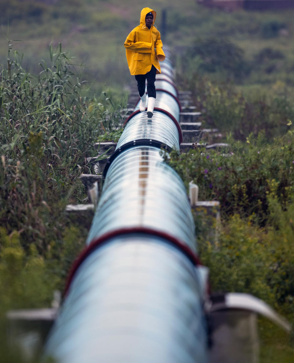 A man runs on top of a sewage pipe at Katlehong, east of Johannesburg, South Africa, Friday, April 3, 2020. South Africa went into a nationwide lockdown for 21 days in an effort to control the spread of the coronavirus. The new coronavirus causes mild or moderate symptoms for most people, but for some, especially older adults and people with existing health problems, it can cause more severe illness or death. (AP Photo/Themba Hadebe)