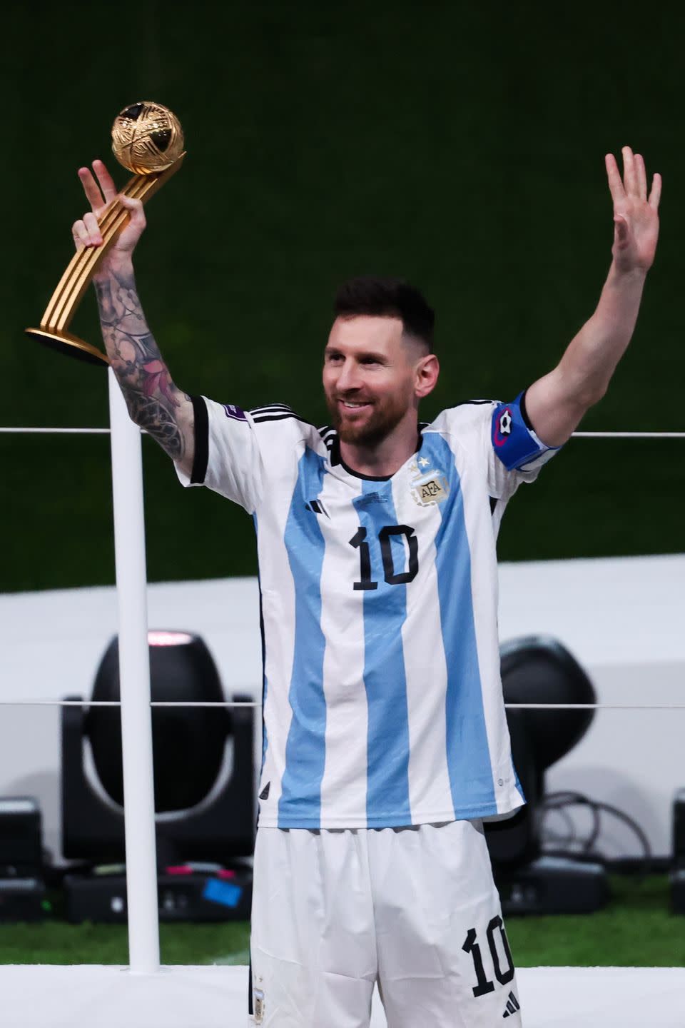 lionel messi holding a trophy with his right hand and waving his arms in celebration