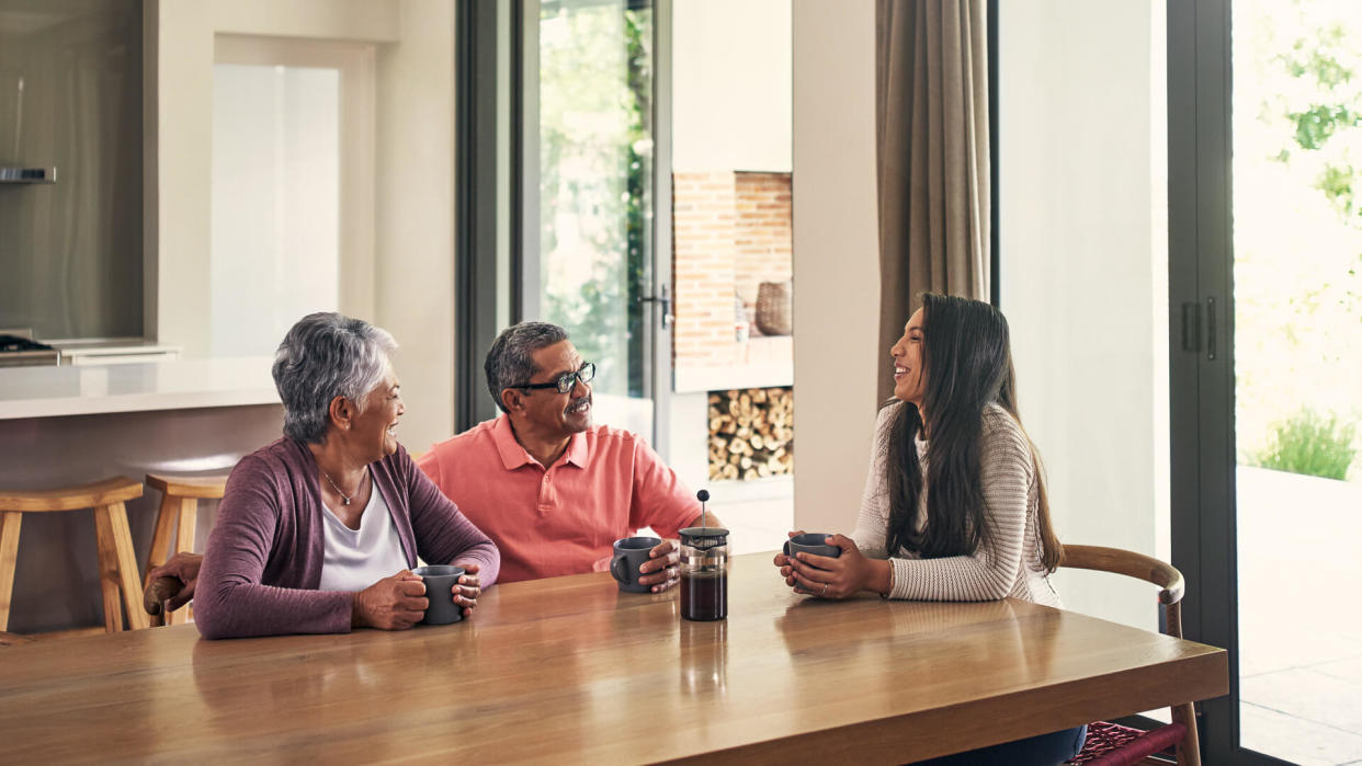 Shot of a young woman chatting and having coffee with her parents at home.