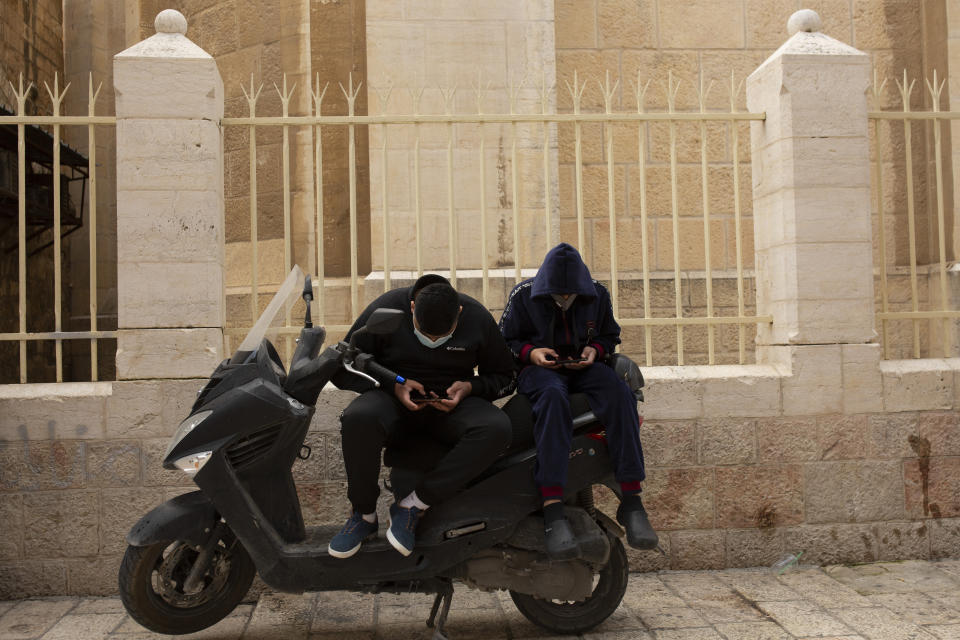 Young men scroll on their smart phones in the Old City of Jerusalem, Wednesday, Dec. 23, 2020. In the early days of the pandemic, a panicked Israel began using a mass surveillance tool on its own people, tracking civilians’ mobile phones to halt the spread of the coronavirus. But months later, the tool’s effectiveness is being called into question and critics say its use has come at an immeasurable cost to the country’s democratic principles. (AP Photo/Maya Alleruzzo)