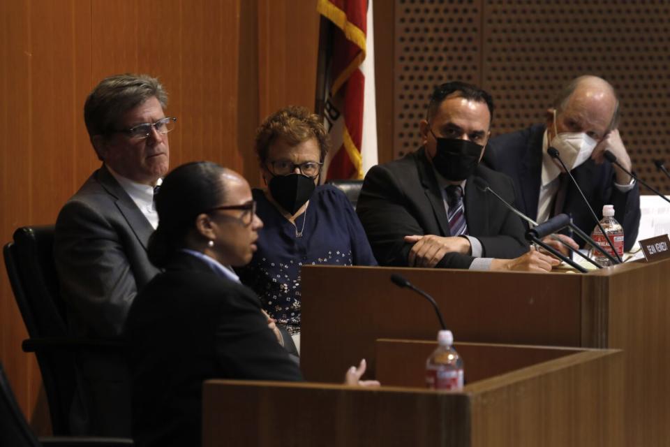 A person speaking on the witness stand as four others look on