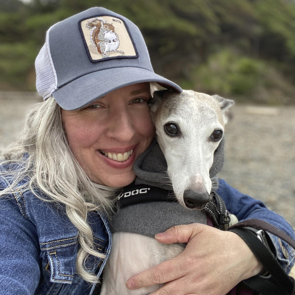 This photo provided by Amy Watson of Portland, Ore., shows her with her dog during a trip to the Oregon Coast in June 2022. Watson, approaching 50, says she has “never had any kind of recovery” from COVID-19. She has had severe migraines, plus digestive, nerve and foot problems. Recently she developed severe anemia. (Amy Watson via AP)