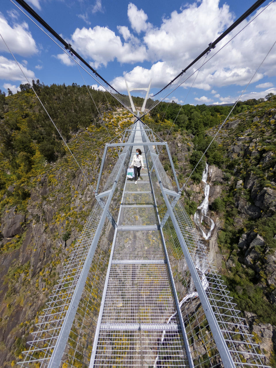 A woman walks across a narrow footbridge suspended across a river canyon, which claims to be the world's longest pedestrian bridge, in Arouca, northern Portugal, Sunday, May 2, 2021. The Arouca Bridge inaugurated Sunday, offers a half-kilometer (almost 1,700-foot) walk across its span, some 175 meters (574 feet) above the River Paiva. (AP Photo/Sergio Azenha)