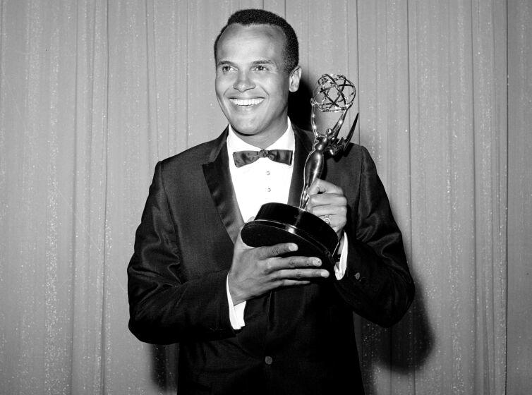 A black-and-white image of Harry Belafonte smiling, wearing a suit and holding an Emmy Award