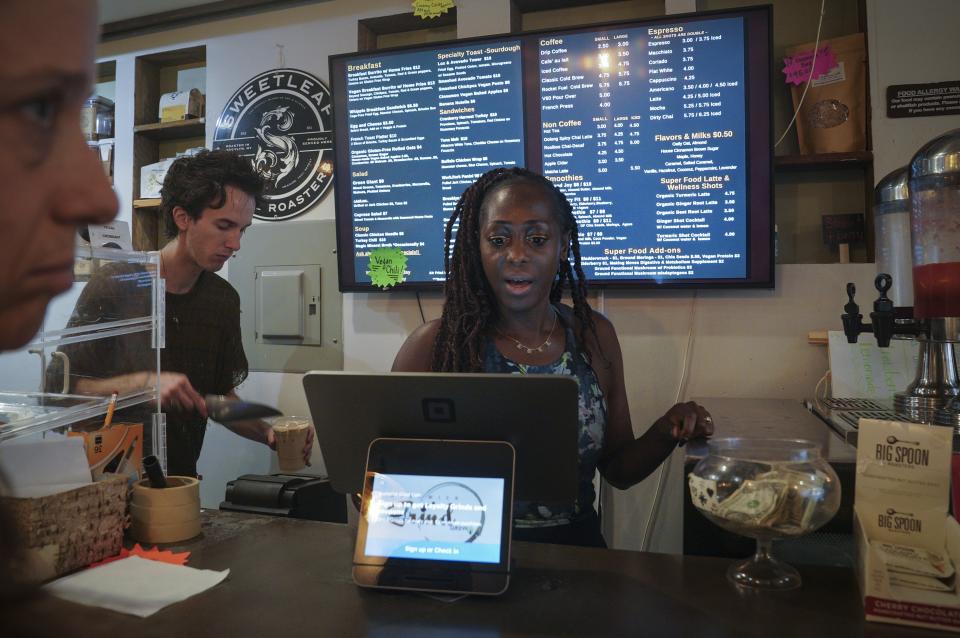 Kymme Williams-Davis, right, takes an order at theBushwick Grind Café she owns, while barista Derek Deyling creates a beverage, Thursday Sept. 8, 2022, in New York. (AP Photo/Bebeto Matthews)