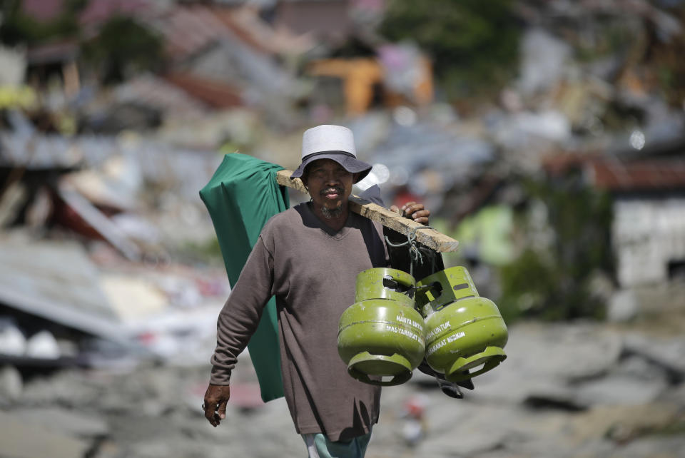 In this Saturday, Oct. 6, 2018, photo, a man carries gas and other items he recovered from toppled homes at the earthquake-hit Balaroa neighborhood in Palu, Central Sulawesi, Indonesia. (AP Photo/Aaron Favila, File)