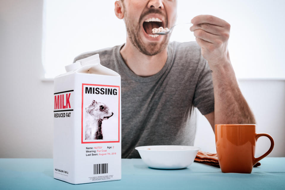 A man eating a bowl of cereal next to a carton of milk on the table with a "Missing" poster on the carton