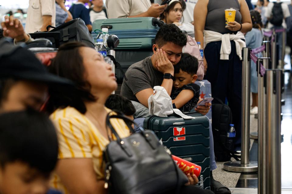 Passengers sitting in a crowded airport, man checking phone for updates