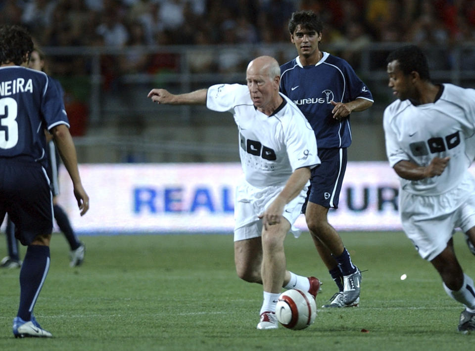 FILE - England's soccer legend Bobby Charlton, center, playing for the Luis Figo foundation team, challenges Laureus foundation players Marco Caneira, left, and Dani, background, during the AllStars charity soccer match, at the Algarve stadium outside Faro, Portugal, July 12, 2004. Bobby Charlton, an English soccer icon who survived a plane crash that decimated a Manchester United team destined for greatness to become the heartbeat of his country's 1966 World Cup-winning team, has died. He was 86. A statement from Charlton's family, released by United, said he died Saturday Oct. 21, 2023 surrounded by his family. (AP Photo/Armando Franca, File)