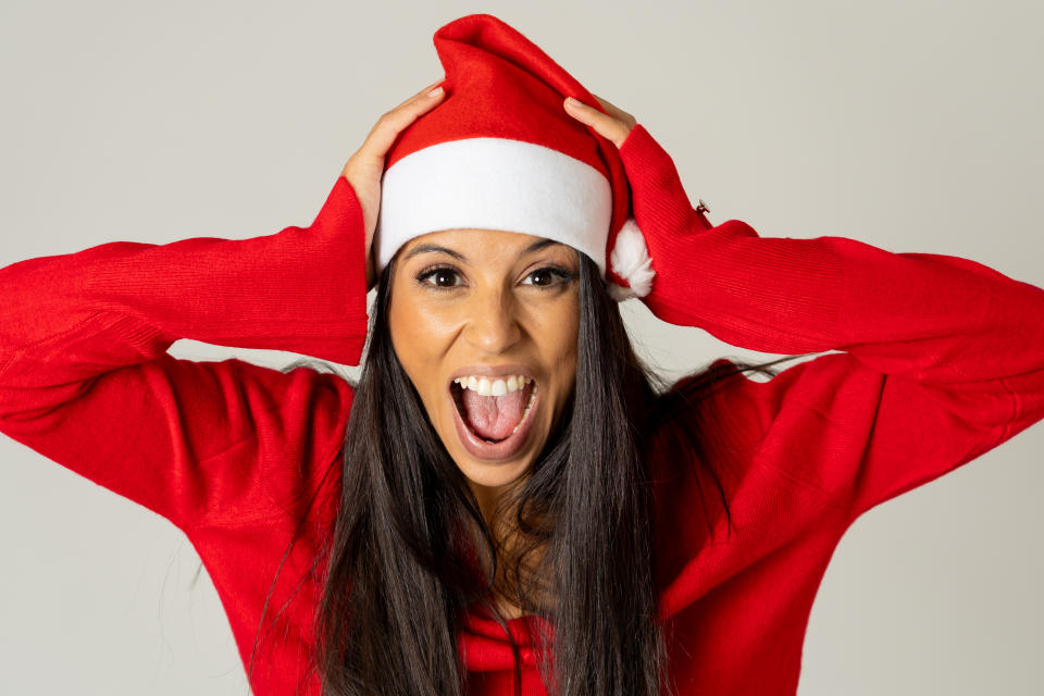 Portrait of a stressed girl wearing red hat looking desperate and angry making gestures isolated on neutral background in christmas is coming not buying present on time overwhelm with family matters.
