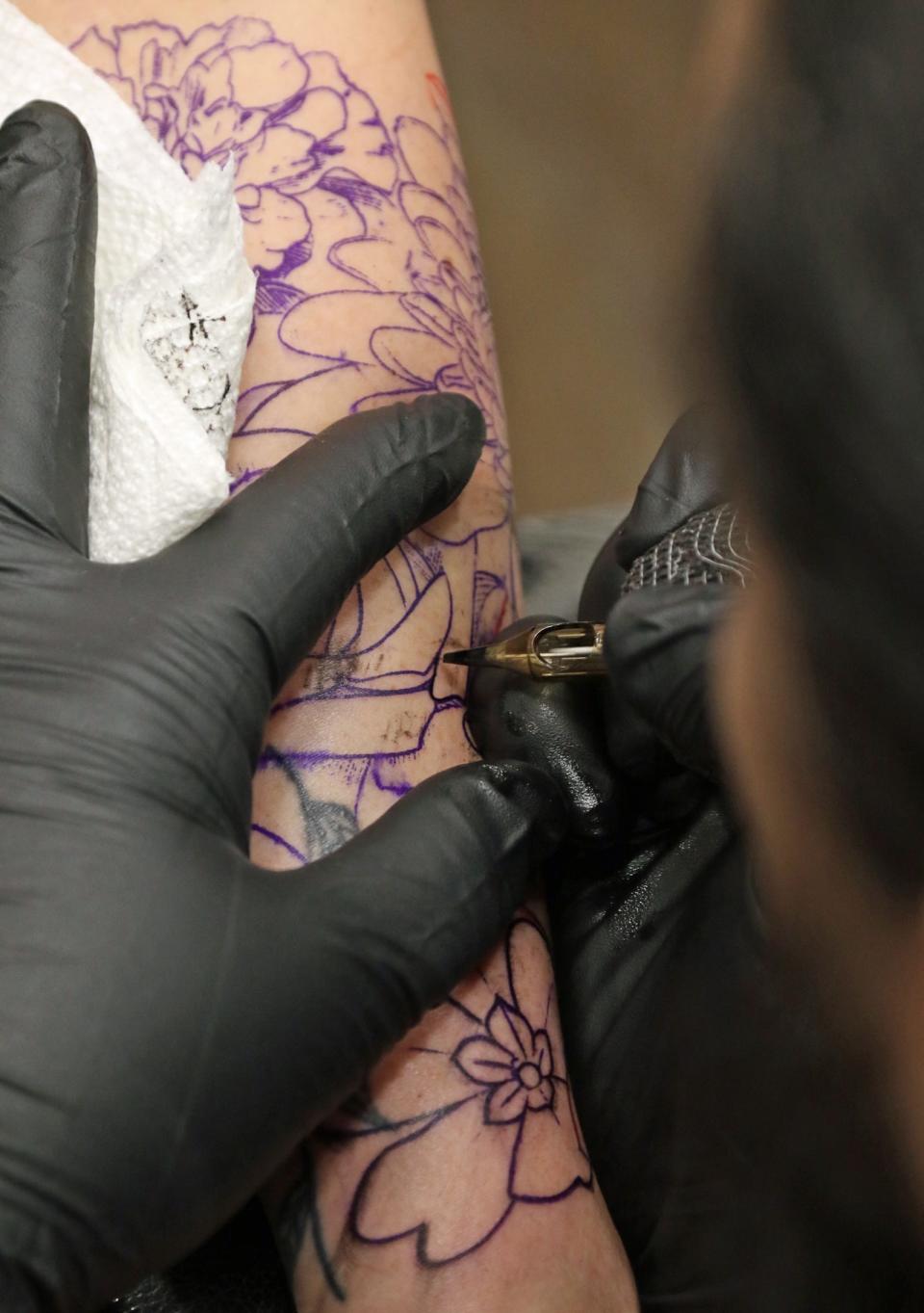 Tattoo artist Dennis Hamilton creates flowers on the arm of Maggie Frazier Saturday afternoon, Jan. 20, 2024, at the Studios on Main Street in Mount Holly.