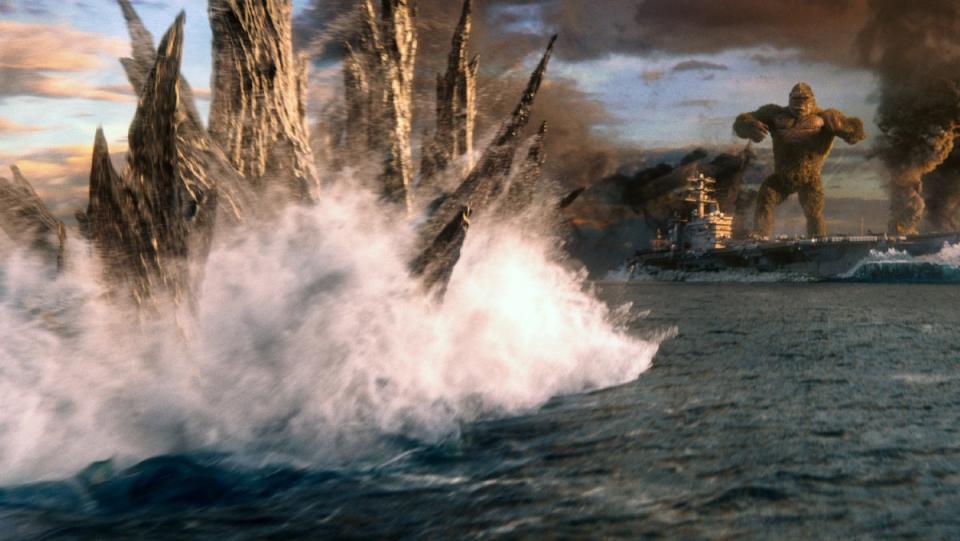 Godzilla swims through the ocean approaching a boat where King Kong stands in a scene from Godzilla vs. Kong.