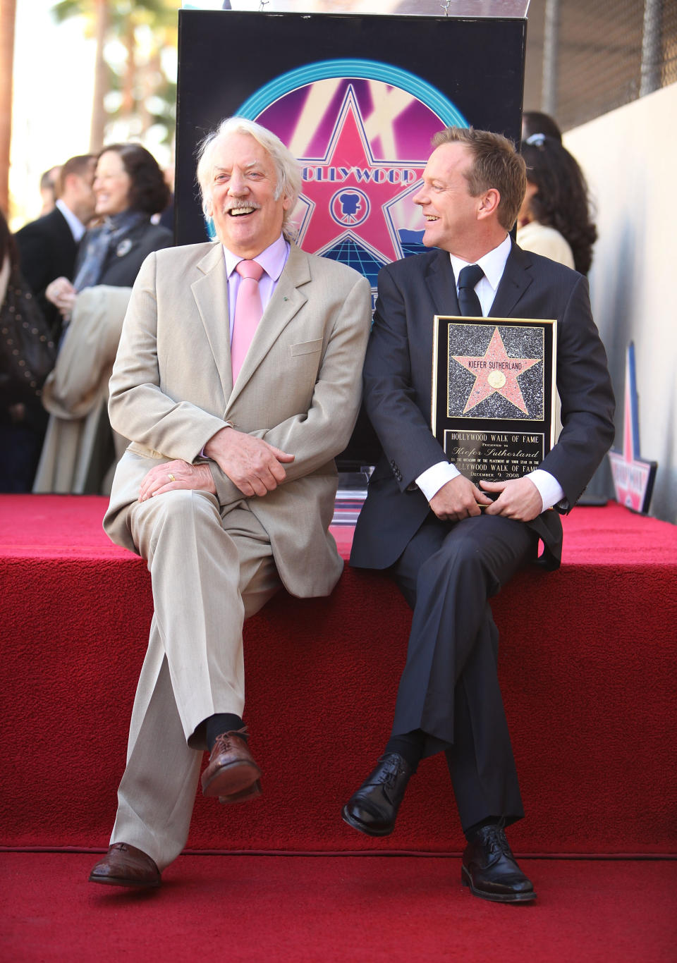 Donald Sutherland and Kiefer Sutherland at a Hollywood Walk of Fame event. They smile as Kiefer holds a plaque