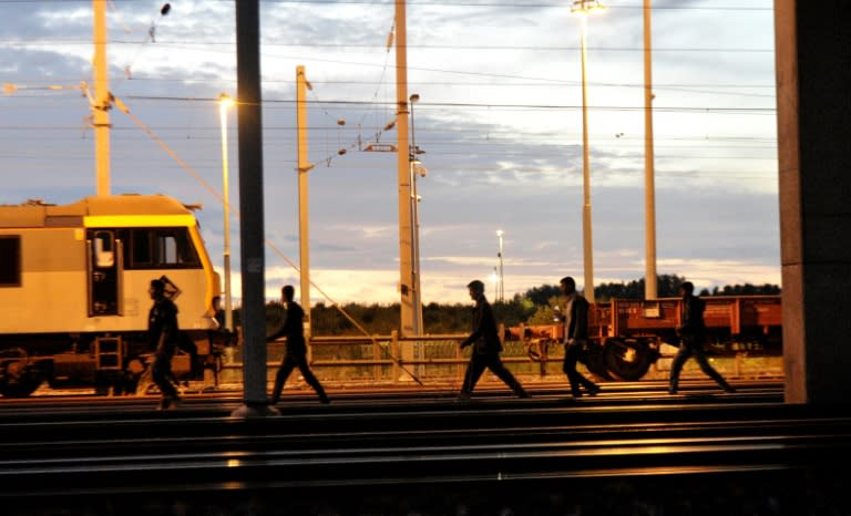 Migrants walk along the railway tracks of the Eurotunnel terminal at the Calais-Frethun station in France on August 10, 2015