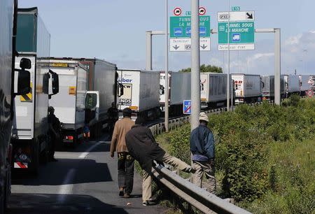 Migrants climb over the barrier to leave the road as French police secure the area as lorries queue in Calais, northern France, July 29, 2015. REUTERS/Pascal Rossignol