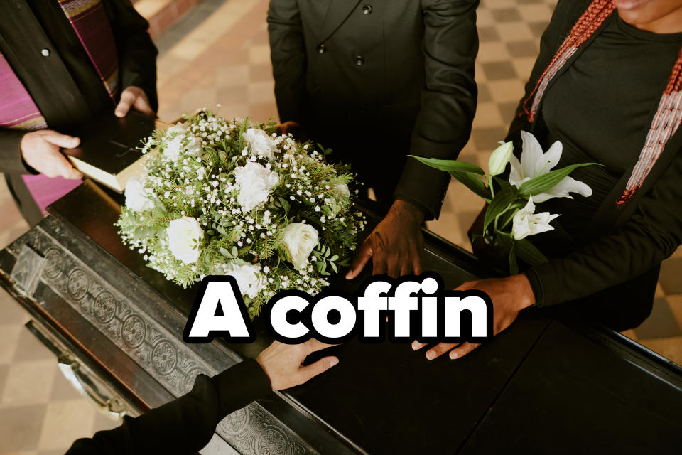 People with hands placed on a casket adorned with a bouquet of white flowers, expressing solemn unity or mourning