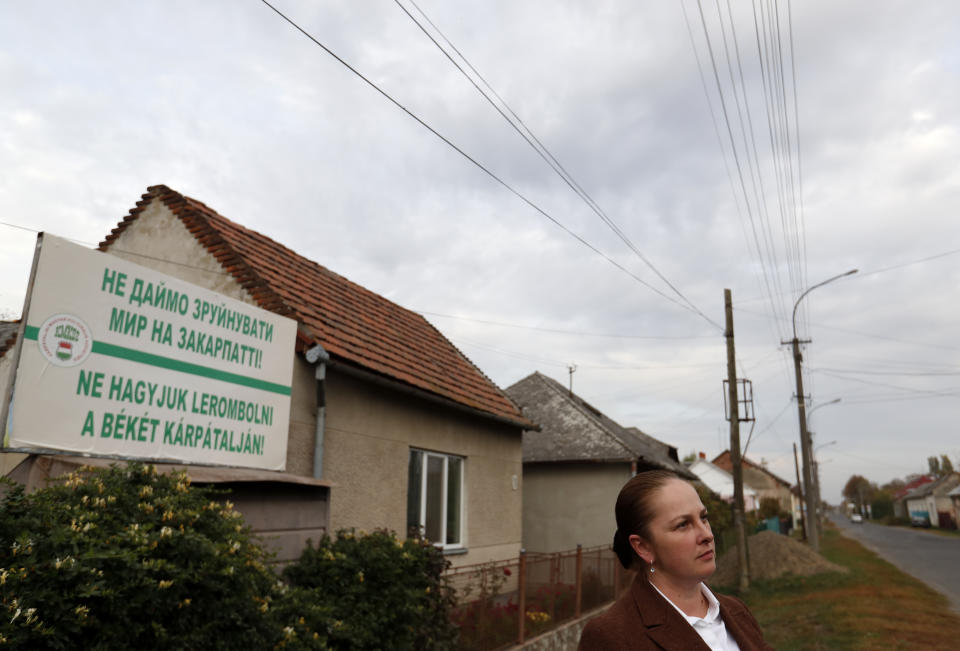 In this Thursday, Oct. 18, 2018, photograph Livia Balogh, an official of the Transcarpathian Hungarian Cultural Association, stands in front of a billboard saying "Let's not allow peace to be destroyed in Transcarpathia!" in Chop, Ukraine. A new education law that could practically eliminate the use of Hungarian and other minority languages in schools after the 4th grade is just one of several issues threatening this community of 120,000 people. Many are worried that even as Ukraine strives to bring its laws and practices closer to European Union standards, its policies for minorities seem to be heading in a far more restrictive direction. (AP Photo/Laszlo Balogh)