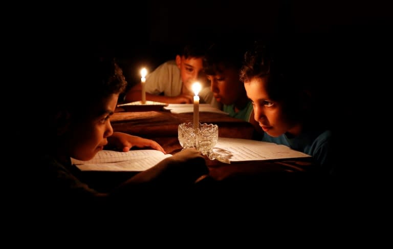 A picture taken on June 13, 2017 shows Palestinian children at home reading books by candle light due to electricity shortages in Gaza City