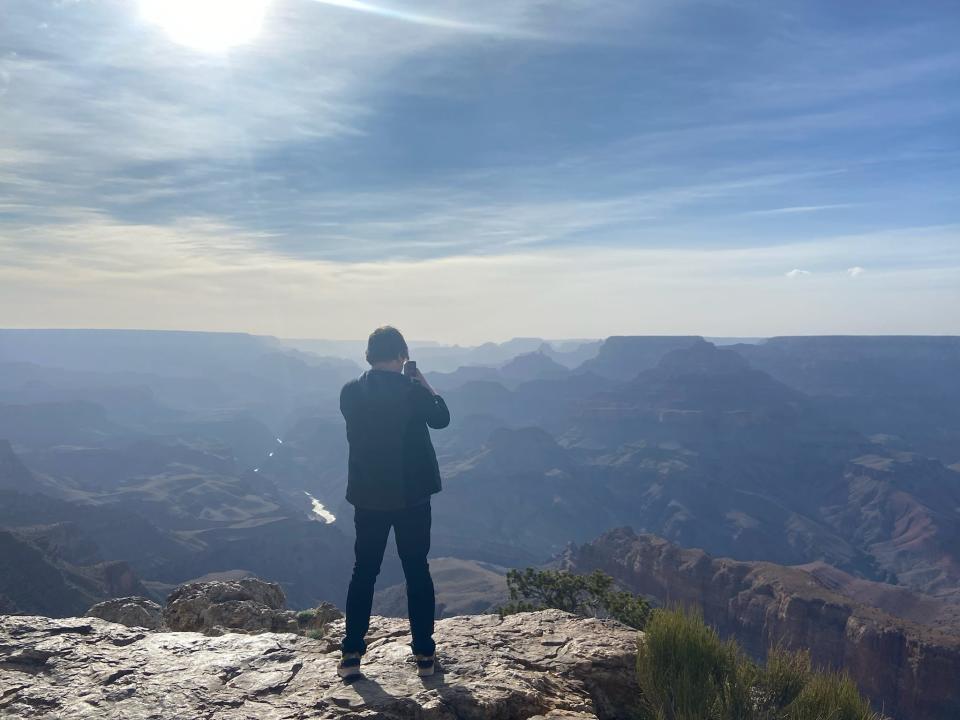 A man standing on the edge of the Grand Canyon taking a photo