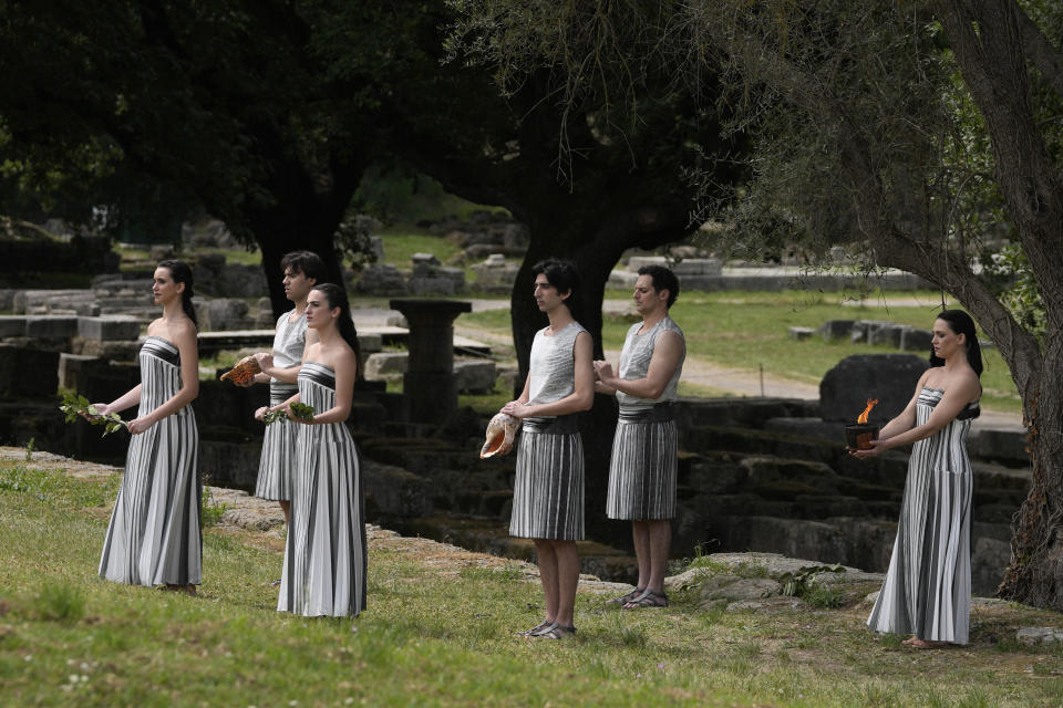 Actress Mary Mina, playing high priestess, right, holds a torch during the official ceremony of the flame lighting for the Paris Olympics, at the Ancient Olympia site, Greece, Tuesday, April 16, 2024. The flame will be carried through Greece for 11 days before being handed over to Paris organizers on April 26. (AP Photo/Thanassis Stavrakis)