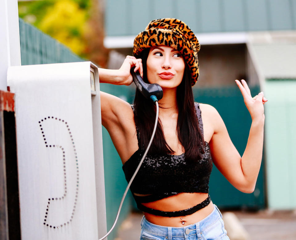 A woman using a payphone and giving the peace sign