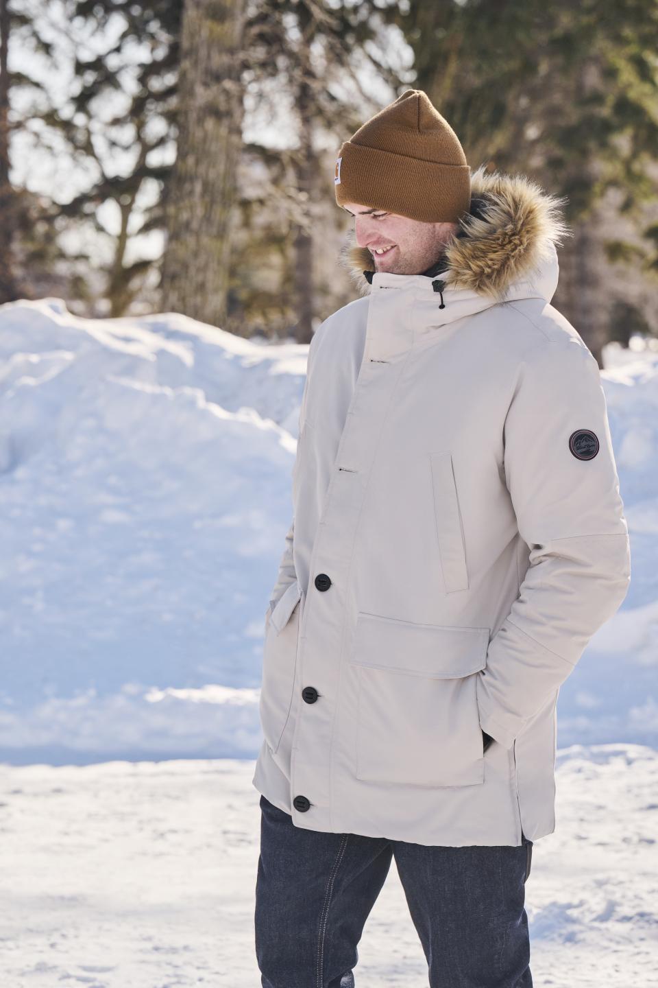 A man is walking outside in the snow in a warm winter parka and Carhartt toque from Mark's