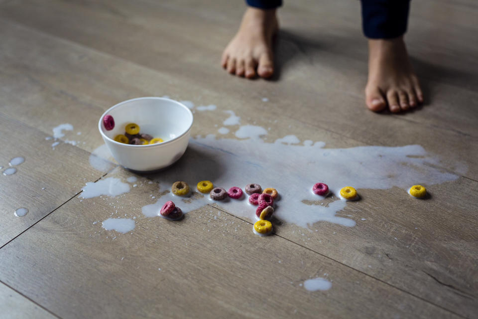 Kinderfuesse und schuessel mit verschuettetem Muesli und Milch auf dem Boden