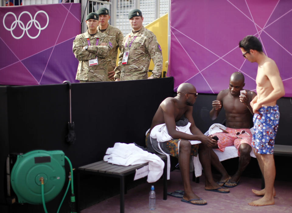 British soldiers stand guard next to dancers awaiting their turn to perform between beach volleyball matches at the London 2012 Olympic Games at Horse Guards Parade