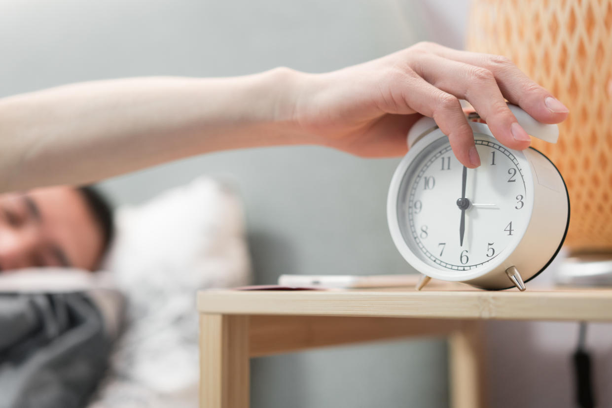 Daylight saving time. Man in bed turning off alarm clock on a nightside table