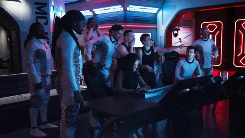 The 'Stars on Mars' cast: 11 people gathered in a dimly lit room with blue and red lighting.