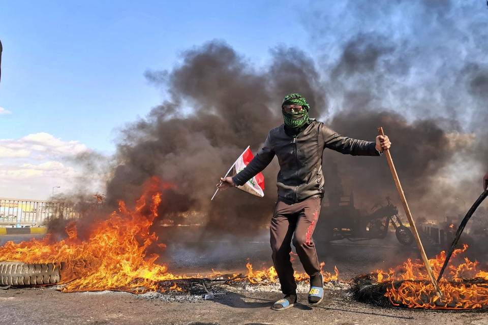 An anti-government protester stands near burning tires set fire to close a street during a demonstration against the newly appointed Prime Minister Mohammed Allawi in Najaf, Iraq, Sunday, Feb. 2, 2020. Former communications minister Mohammed Allawi was named prime minister-designate by rival Iraqi factions Saturday after weeks of political deadlock. (AP Photo/Hadi Mizban)