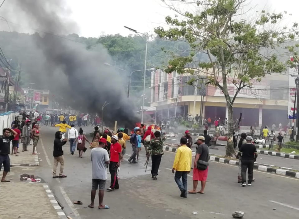 People gather on a street as smoke billows from a burning car during a violent protest in Manokwari, Papua province, Indonesia, Monday, Aug. 19, 2019. The protest was sparked by accusations that Indonesian police who backed by the military, have arrested and insulted dozens of Papuan students in their dormitory in East Java's cities of Surabaya and Malang a day earlier. (AP Photo/Safwan Ashari Raharusun)