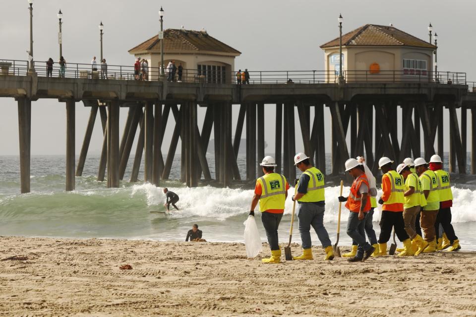 Clean-up crews continue to comb the beach as surfers were allowed back in the water near the Huntington Beach Pier