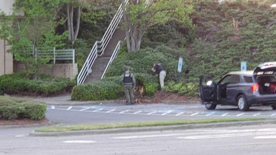 A police canine unit searches for evidence in brush outside Carolina Place mall after a gunfight inside the Pineville shopping center on Saturday, May 1, 2021.