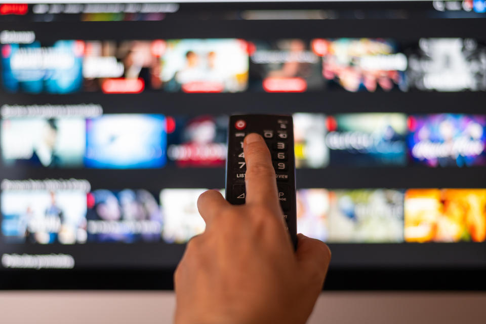 Hand using a remote to select a program on a smart TV screen