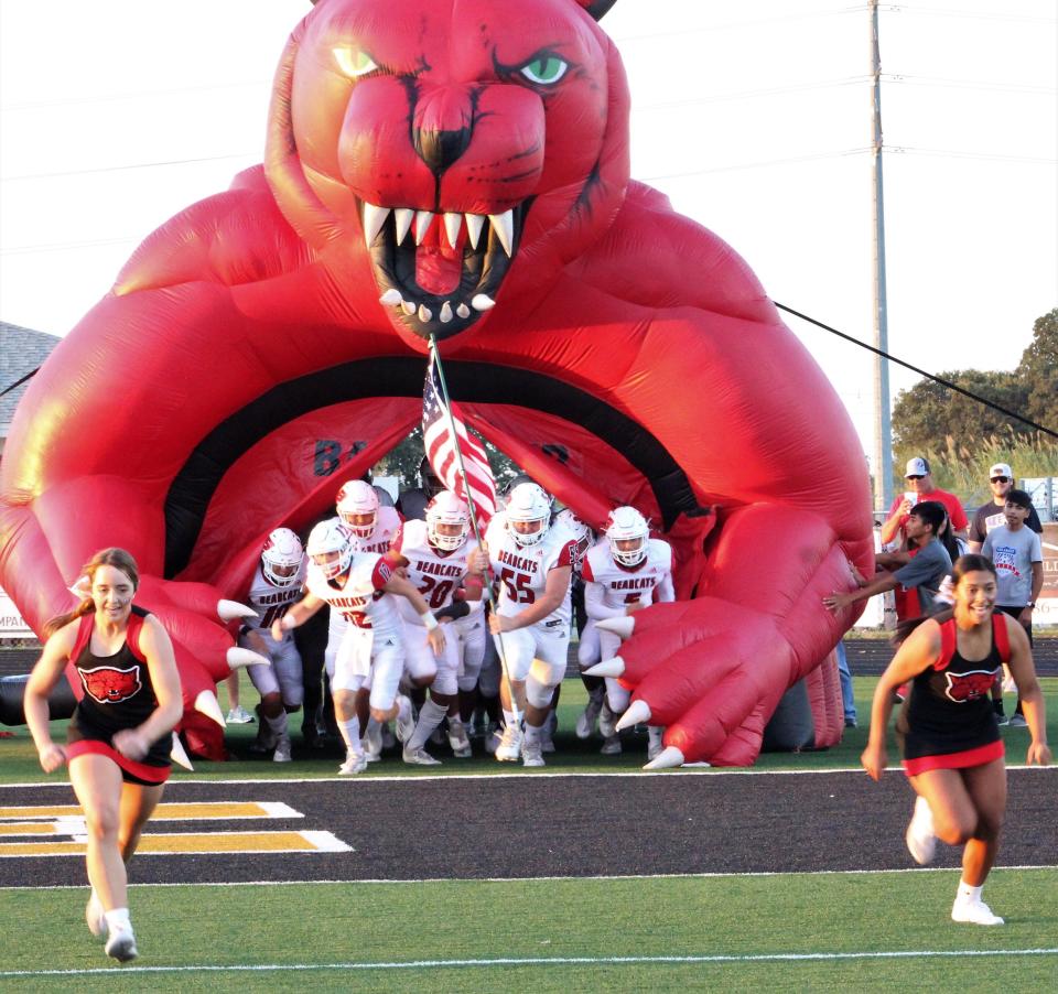 The Ballinger football team bursts from its Bearcats inflatable lead by two cheerleaders to enter Bulldog Stadium field on Sept. 17, 2021.