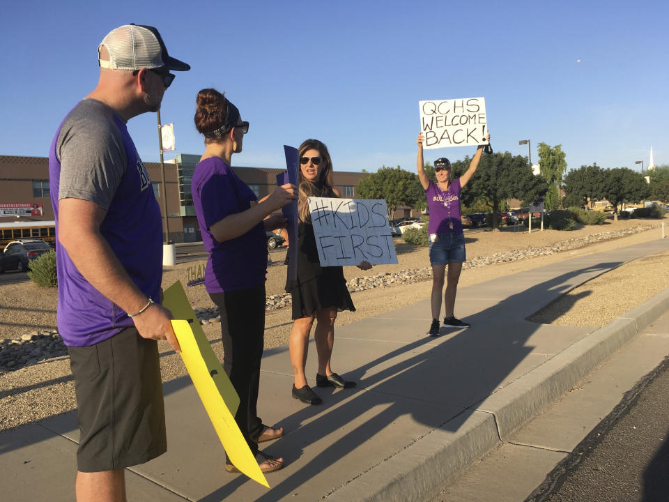 Michael Bayard, far left, Ashleigh Bayard, Shelli Boggs and Dawn Oliphant, hold signs outside Queen Creek High School in Queen Creek, Ariz., on Monday, Aug. 17, 2020 to welcome students back on the first day of school. The first day of school, a normally happy ritual, was fraught with conflict Monday at some schools opening in Arizona, echoing debates across the country over the risks of holding all in-person instruction amid the coronavirus pandemic. (AP Photo/Terry Tang)