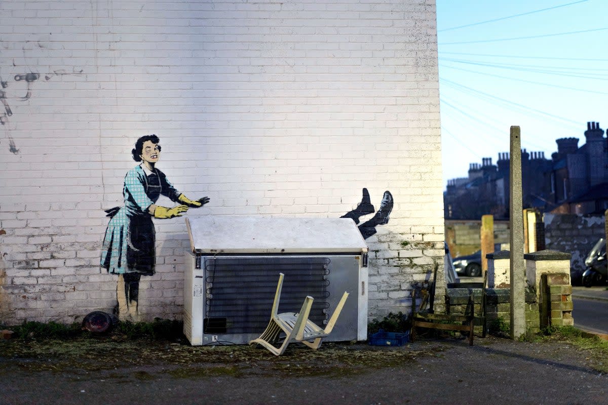 14 February 2023: One of the new works by Banksy, appears to show a 1950’s housewife, wearing a classic blue pinny and yellow washing up gloves, with a swollen eye and a missing tooth seemingly shoving her male partner into a chest freezer, the piece is set on a white wall backdrop in Kent (PA)