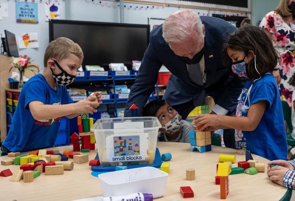 President Biden leans down to talk to pre-K students around a table with building blocks.