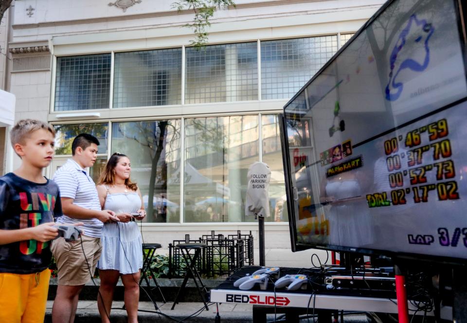 Brone McDonald, 9, from left, Shery Chao and Alexis Diaz play video games from the Carcade set up at the Milwaukee Night Market along West Wisconsin Avenue on August 18, 2021.