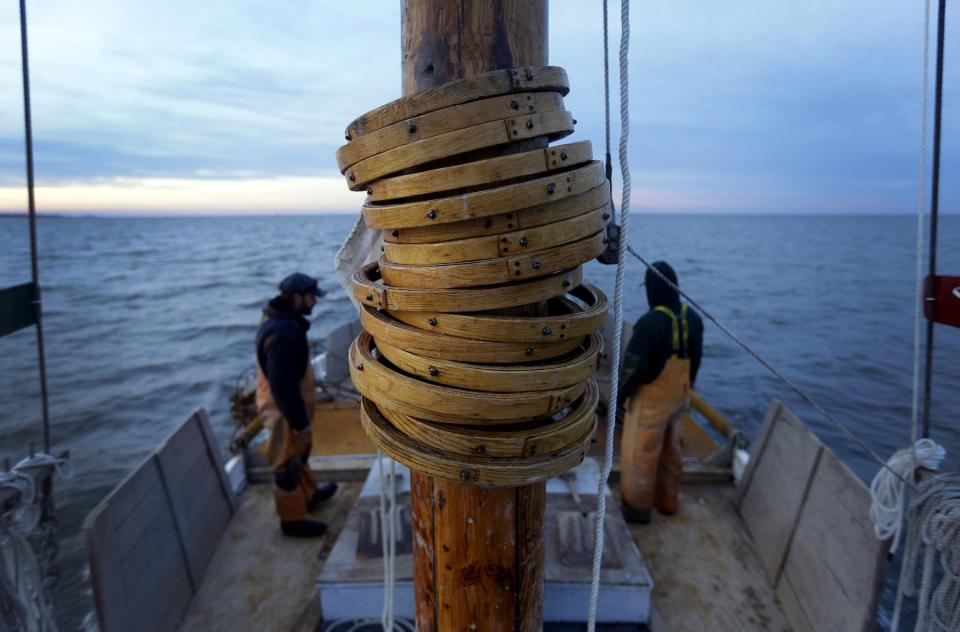 In this Dec. 20, 2013 picture, wooden hoops attached to the mainsail rest on the mast of the skipjack Hilda M. Willing as Shawn Sturgis, back left, and Danny Benton prepare for a day of oyster dredging in Tangier Sound near Deal Island, Md. While the skipjack was the vessel of choice for oystermen who made their living on the Chesapeake Bay around the turn of the 20th century, today only a handful are used for commercial dredging during Maryland’s oyster season. (AP Photo/Patrick Semansky)