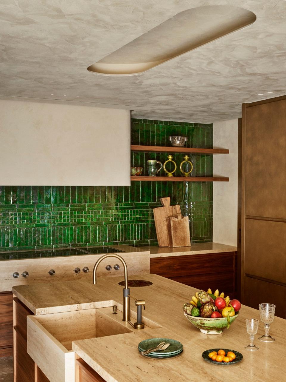 The kitchen built-in storage was made out of travertine, oak wood, and walnut. The credenza is adorned with green Moroccan zellige handmade enamel tiles.