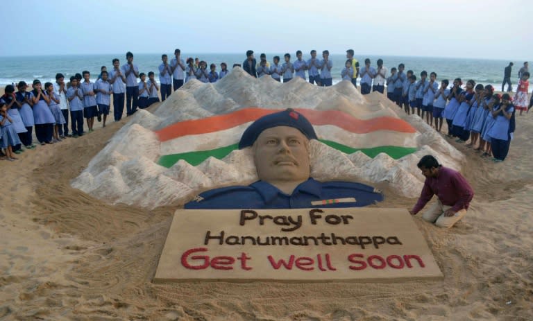 Indian students pray near a sand sculpture created by Sudarsan Pattnaik of Hanumanthappa Koppad, rescued after five days after being buried in an avalanche in the Himalayas, at Puri beach, on February 10, 2016