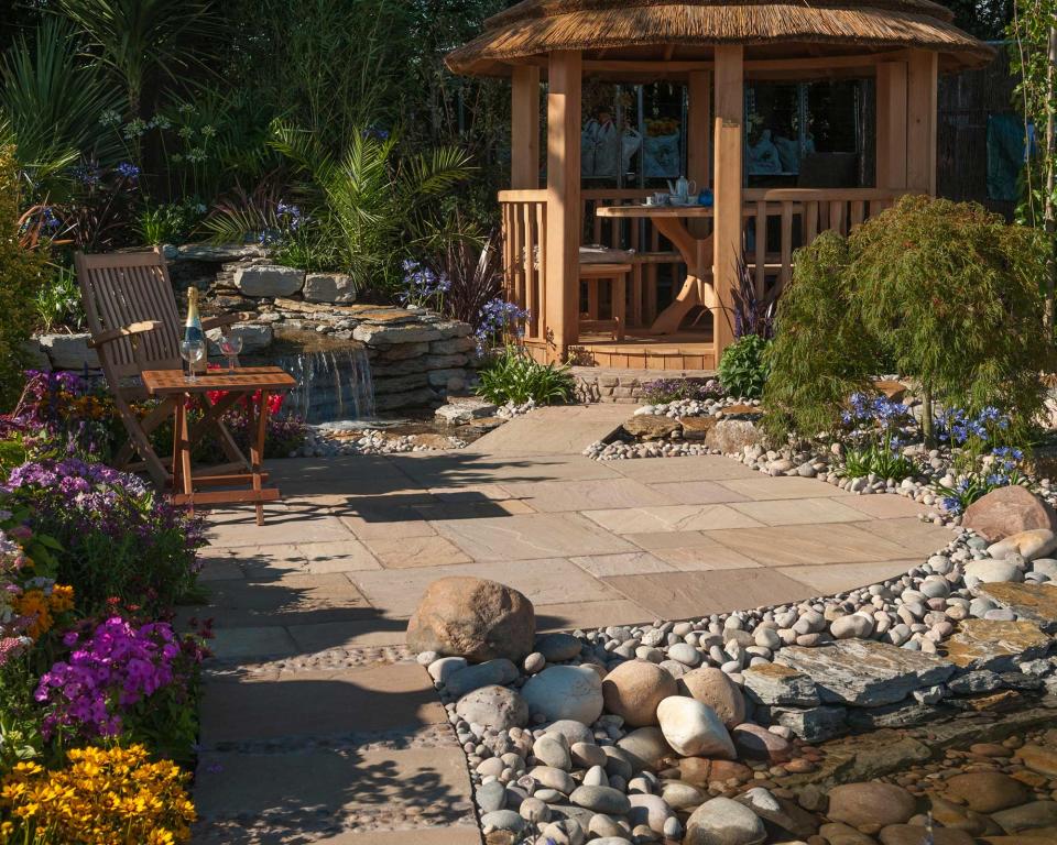 <p> Pick river rocks in a hue to complement your paving for the perfect border for your patio. They offer an almost Mediterranean-style vibe to this space, especially alongside hot-hued blooms to the left, and the soothing waterfall and spiky foliage behind. </p> <p> Drought-tolerant plants, such as agapanthus, will thrive in stony surroundings, so consider bringing some into your scheme for extra visual interest. We love the gazebo in this plot, too – the ideal spot for whiling away a summer's afternoon with a glass of something cold or a cup of tea. </p>