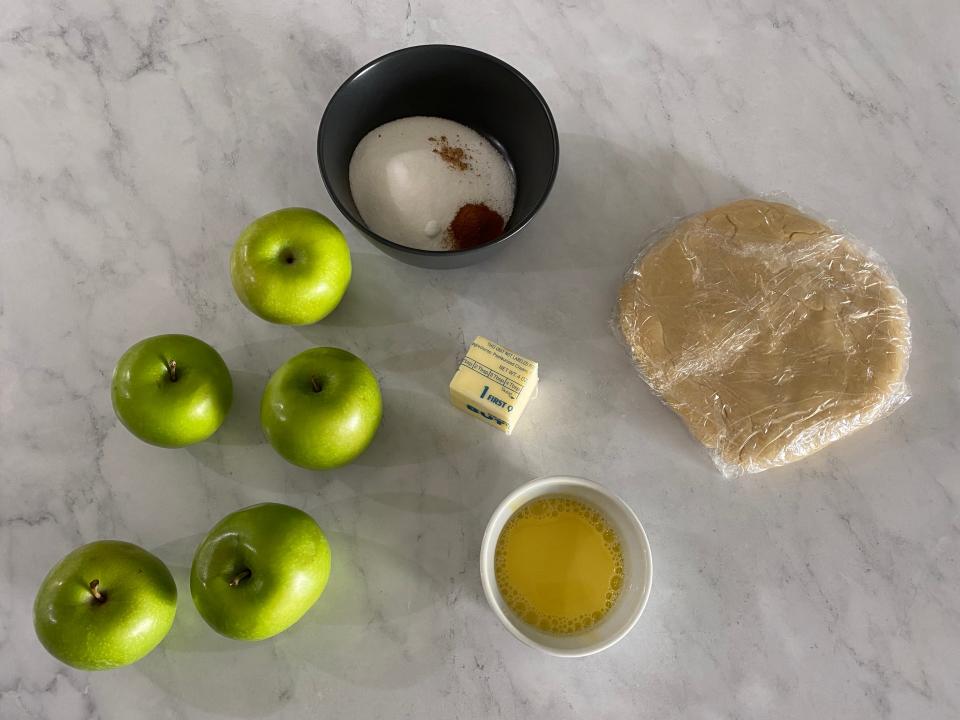 Flat lay of green apples, sugar, butter, dough, and egg yolks.