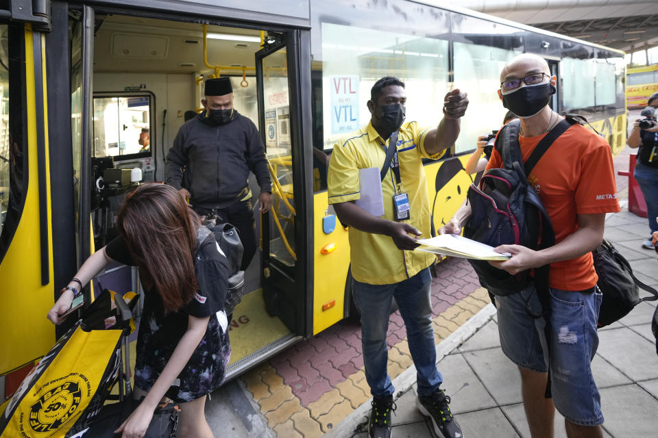 A bus operator checks the ticket of passengers at Larkin bus station in Johor Bahru, Malaysia, Monday, Nov. 29, 2021. Malaysia and Singapore partially reopen their borders Monday for fully vaccinated citizens and some others, after nearly two years of closure due to the pandemic that had stranded many Malaysians working in the neighboring city-state away from their families. (AP Photo/Vincent Thian)