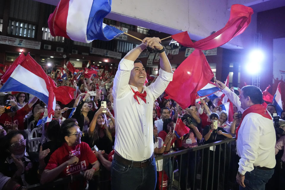 Santiago Peña, centro, candidato presidencial del partido Colorado, y el expresidente Horacio Cartes, derecha, sostienen las banderas de Paraguay y del partido en un mitin político en Asunción, Paraguay, el lunes 24 de abril de 2023. Las elecciones generales de Paraguay están programadas para 30 de abril. (Foto AP/Jorge Sáenz)