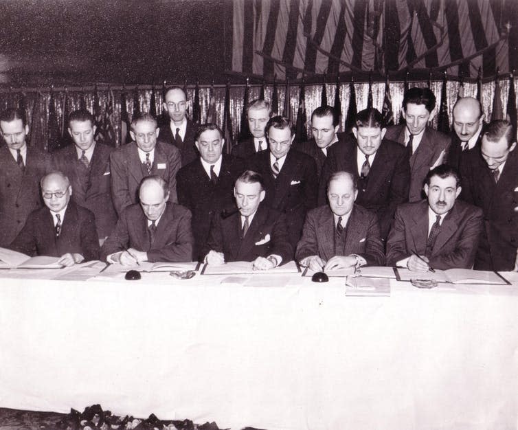 A black-and-white photograph of men standing around a table.